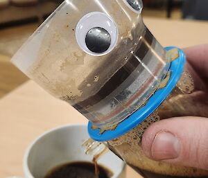 Coffee is poured out of a contraption with googly eyes on it, into a cup