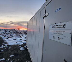 A non-descript shipping container on a rocky and snowy slope