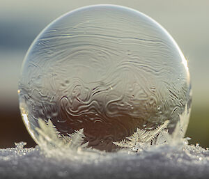 A clear soap bubble with white ice crystals forming snowflake patterns at the base