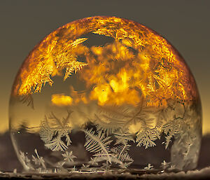A soap bubble with frosty patterns lit up in bright yellow from the rising sun behind