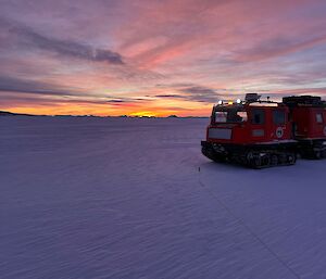 A big red tractor on ice under a dawn or dusk sky