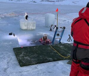 A person in red stands in front of a hole cut in the ice