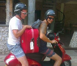 Two young men on a red moped wearing helmets
