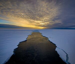 A deep dark swathe cuts through the ice, presumably behind the ship,  under a dawn or dusk sky