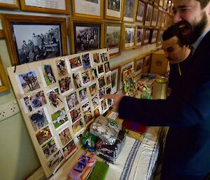 two men stand looking at table covered with cloth and then wrapped gifts, including one board covered with photos of pets