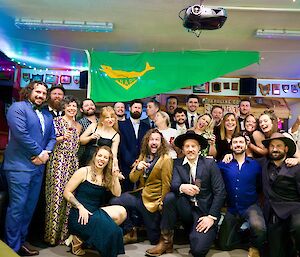 A group of 24 people in cocktail attire look to camera and smile, above hangs the ANARE flag