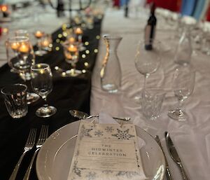 Table setting with cutlery, crockery and glass wear and then many candles down the middle of the table. Midwinter menu sits on top of the plate.
