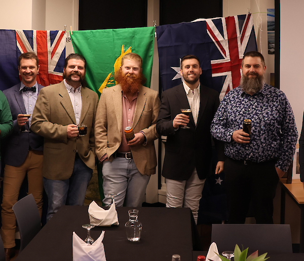7 diesel mechanic expeditioners proudly pose afront the Australian flag, new Zealand flag and the ANARE flag