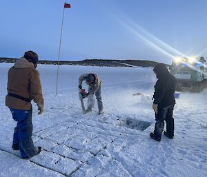 Three expeditioners on the sea ice in Horseshoe Harbour, one with a chainsaw cutting the ice blocks