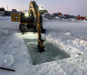 The excavator makes the final break in a chain-saw cut hole to allow sea water to fill the pool for the Mawson Midwinter swim