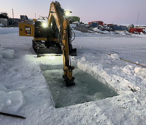 The excavator makes the final break in a chain-saw cut hole to allow sea water to fill the pool for the Mawson Midwinter swim