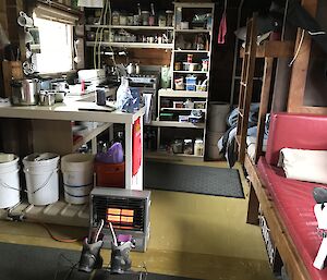 Inside of hut showing kitchen area with well stocked shelves, and bunk beds down right hand side