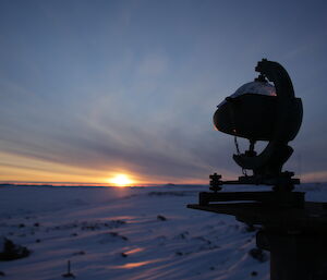 A sun rises over snow, with a sunlight recording instrument in the foreground.