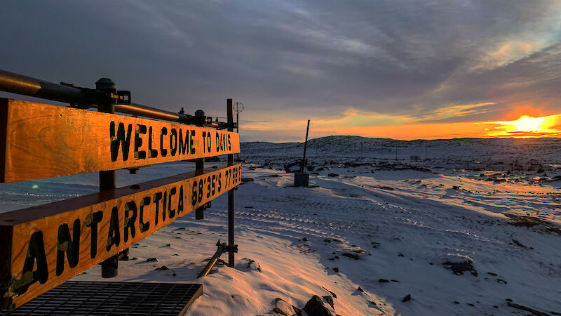 A sunrise casts an orange glow on a wooden sign saying 'Welcome to Davis'.