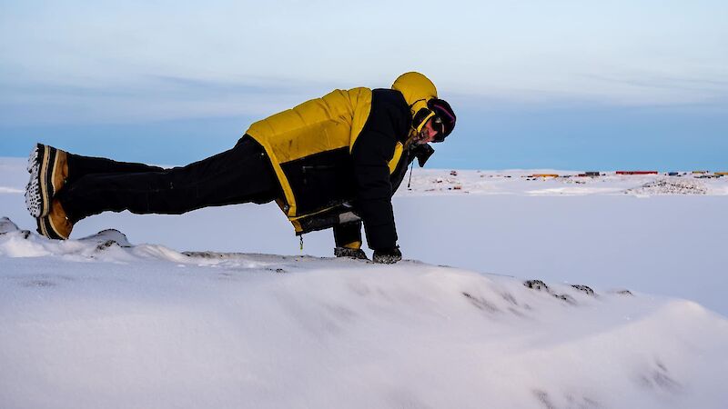 A man in yellow winter clothing doing a push up in Antarctica