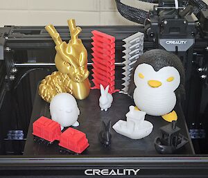 Acollections of 3D printed objects printed on station, including a golden dragon, a model Hagglunds, penguins, bunnies and a tugboat.