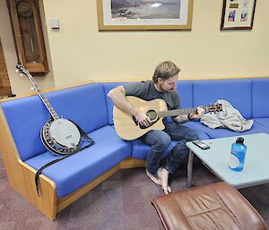 An expeditioner playing guitar upstairs in the Mawson lounge