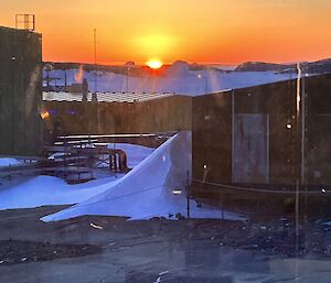 An orange and yellow sunrise with the golden half circle of the sun on the horizon near Mawson station.