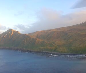 Looking across the sea from an aircraft at a mountain range with small hut on a ridge line about a third of the way up