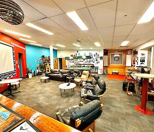 A large room with lounge chairs and a movie screen, red and aqua feature walls and a pool table