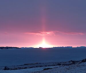 The sun just above the horizon with snowy slopes in the foreground