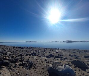 A bright sun above a rocky foreground with a lake in the background