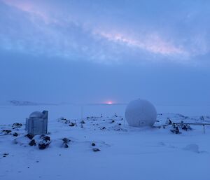 Snowy landscape under a pale grey sky with a radome in the foreground