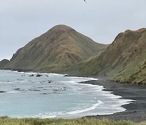 A black sand beach and brown/green hills in the background