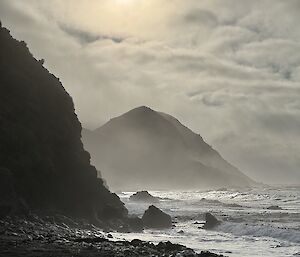 Sunlight above a rough sea and a rocky beach with steep headlands