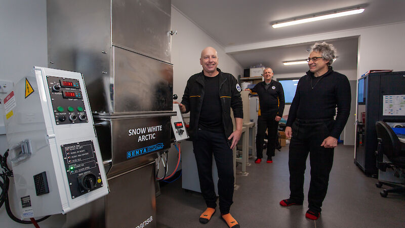 Three men in black stand in a laboratory