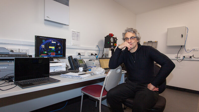 A man in black sits at a chair in front of a computer