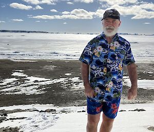 A man in a bright shirt stands on a rock with snow behind him