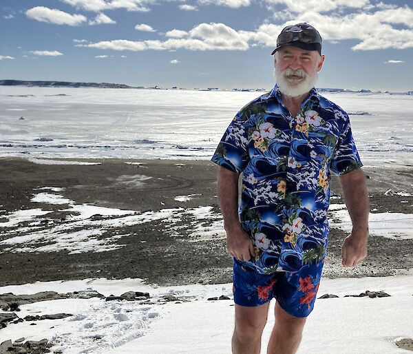 A man in a bright shirt stands on a rock with snow behind him