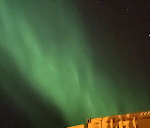 A green aurora australis above a yellow shed