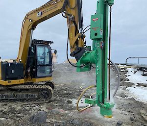 A yellow bulldozer with a green drill bores into the ground