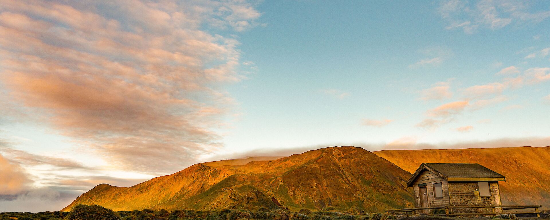Beautiful golden light hits the south end of station where there is a small unused hut and then the mountains raise up behind