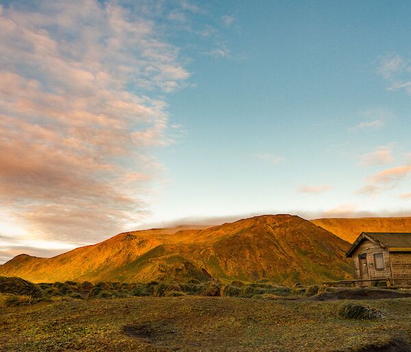 Beautiful golden light hits the south end of station where there is a small unused hut and then the mountains raise up behind