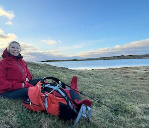 Woman sits beside field pack on the side of a lake