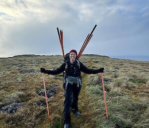 Woman with field pack on with track markers sticking out stands and smiles at camera