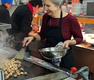 Woman in apron cooks scallops on a large hotplate