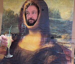 Large print of the Mona Lisa painting with face removed and then person putting face through the hole made