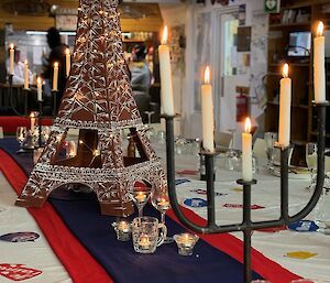 Large dinner table set with white tablecloth and blue and red runner down the center, with a replica of the Eiffel Tower in the middle with candelabra and tealights either side