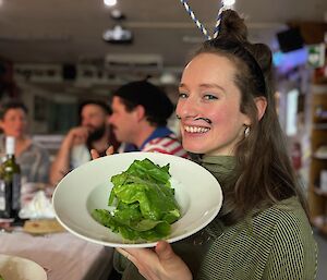 Woman dressed as a snail with antennae on head smiles and she holds up a plate of lettuce