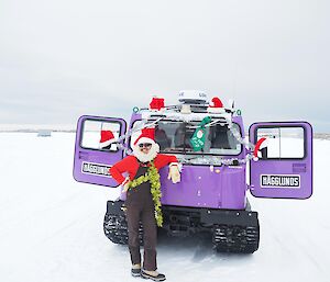 Alex in front of purple hagg with a large variety of Santa Christmas decorations on himself and also the hagg