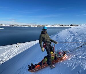 Alex wrangles a mock patient transfer vertical stretcher lift during a search and rescue training session. snowy filled hilled and a great big open O'Brien bay in the background