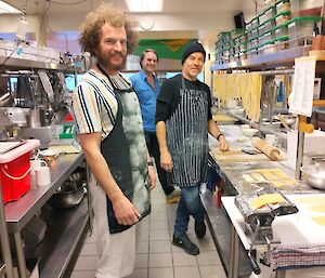 Three men stand in a kitchen preparing pasta