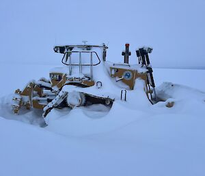 A bull dozer is pictured covered heavily with snow after a strong weather event. Grey cloud backdrop sky.