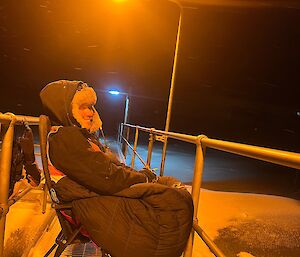 An expeditioner wrapped in a sleeping bags sits patiently atop the fuel storage tanks with blowing snow during the middle of the night waiting for the next tank level dip.