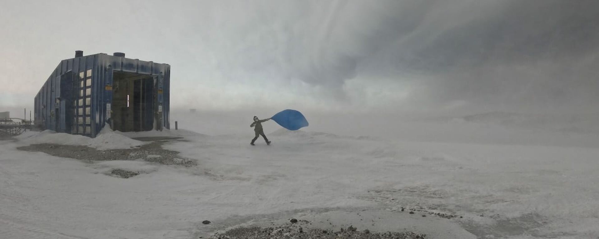 A person, to the right of a building, launches a blue balloon into the sky