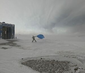 A person, to the right of a building, launches a blue balloon into the sky